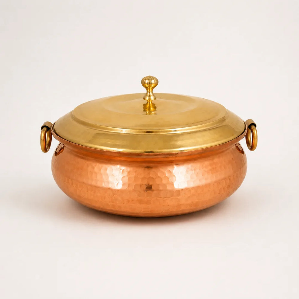 Nutristar hammered copper biryani handi with brass lid, decorative knob and side ring handles on off-white background