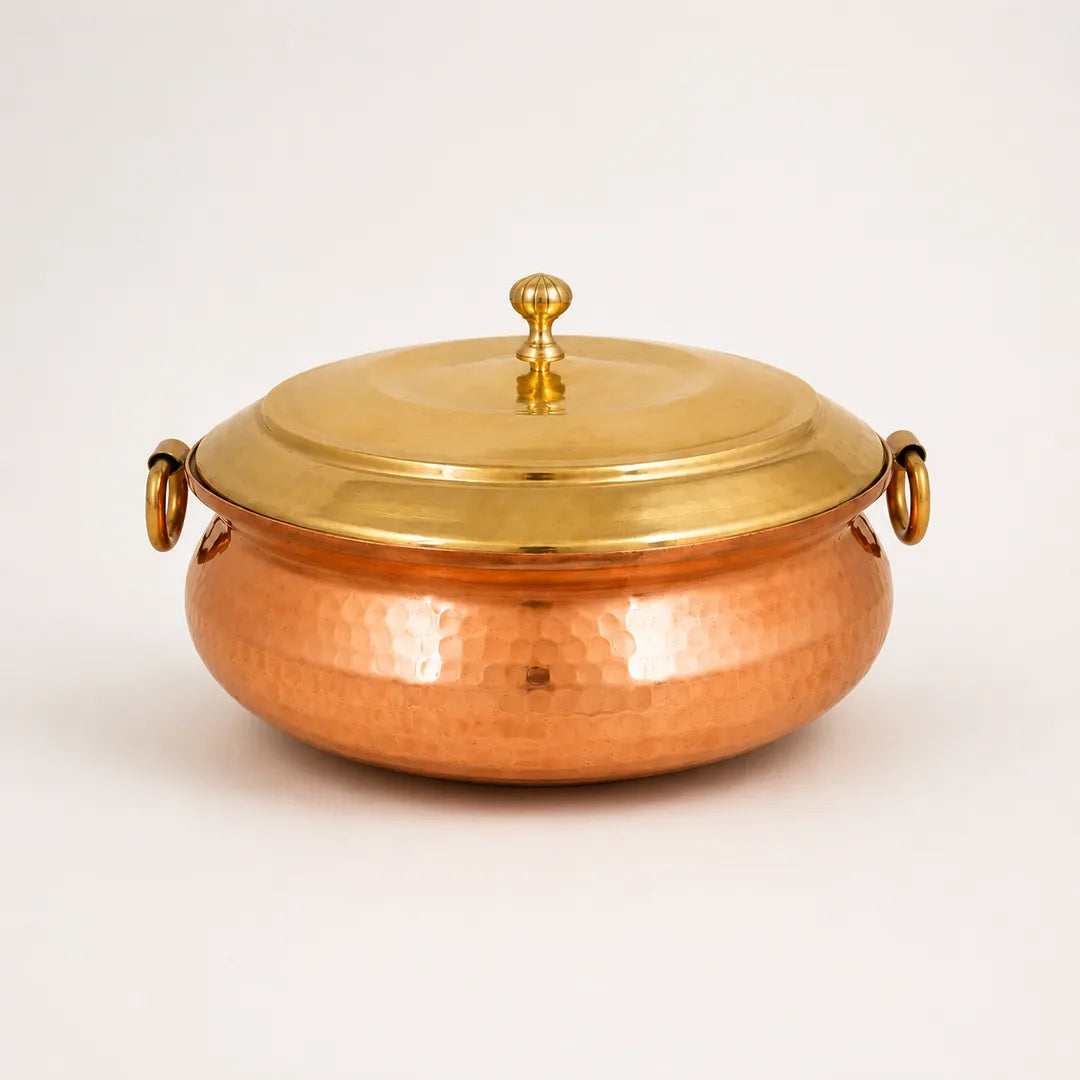 Nutristar hammered copper biryani handi with brass lid, decorative knob and side ring handles on off-white background